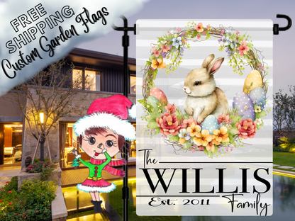 Bunny-and-floral-wreath garden flag with pastel Easter eggs and Willis family name, shown outside a house at dusk.