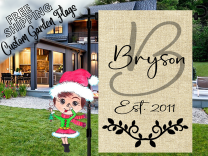 Burlap-look garden flag with a sage B monogram, Bryson name, establishment year and black leafy flourish outside a house.