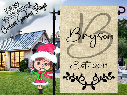 Burlap-look garden flag with a sage B monogram, Bryson name, establishment year and black leafy flourish beside a white house.