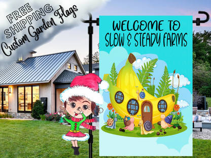 Slow and Steady Farms garden flag mockup with a yellow cottage, snails and flowers, shown beside a white house.
