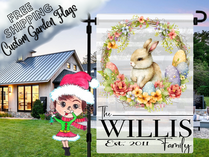Bunny-and-floral-wreath garden flag with pastel eggs and Willis family name, shown beside a white house.