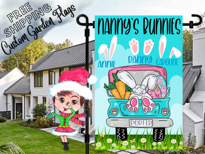 Nanny's Bunnies garden flag with named bunny-ear and paw motifs above a turquoise truck on blue in a daytime yard.
