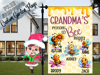 Grandma’s Reasons to Bee Happy garden flag with five named cartoon bees, colorful flowers, a purple heading and honeycomb design. Close-up beside a porch.