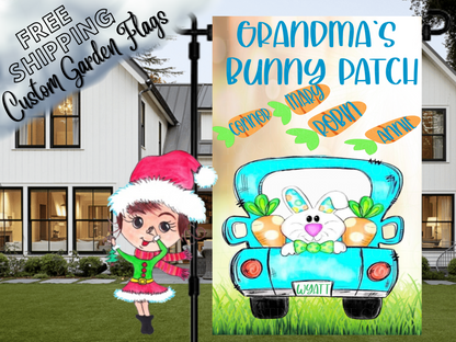Close-up Grandma's Bunny Patch garden flag with a turquoise truck, bunny and named carrots, shown by a porch.