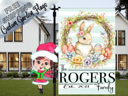 Close-up Rogers family garden flag with bunny, floral wreath and Easter eggs, displayed in front of a porch.
