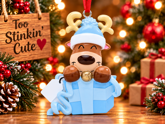 Reindeer in a light blue gift box Christmas ornament wearing a blue winter hat, displayed in a rustic holiday scene.