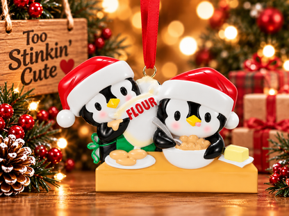 Penguin pair preparing cookie dough with a silver-colored spoon and a plate of cookies beside the mixing bowl.