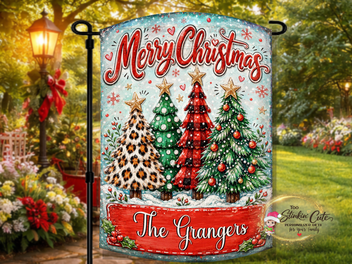 Whimsical holiday garden flag featuring four unique Christmas trees, a snowy blue background, Merry Christmas lettering, and a personalized red family name plaque.