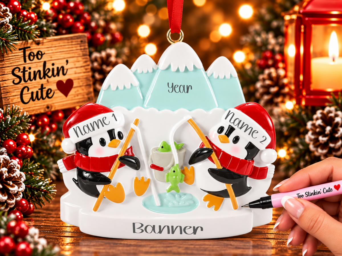 Penguin couple ornament with orange fishing poles, green fish, and a light blue ice fishing hole.