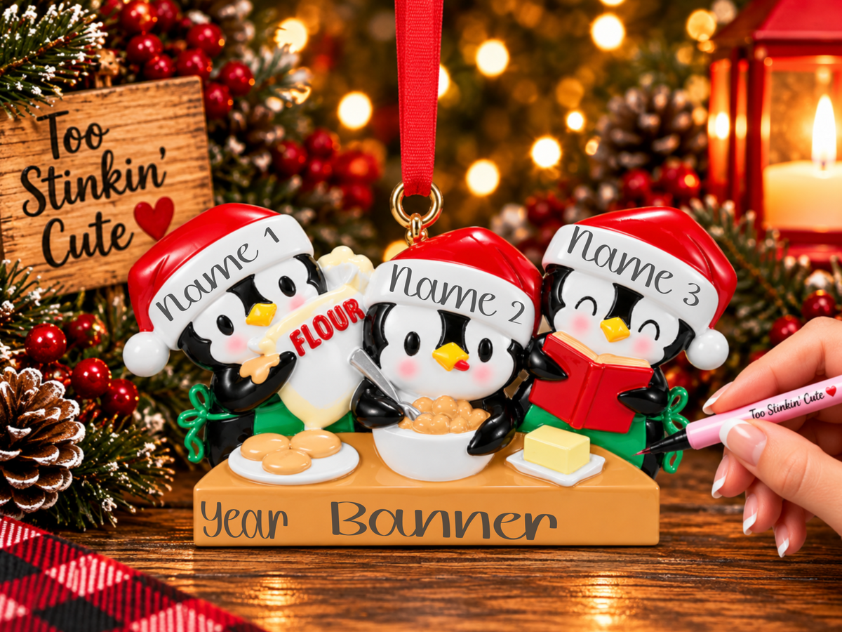 Penguin family of three baking ornament with a flour bag, mixing bowl, red recipe book, cookies, and butter.