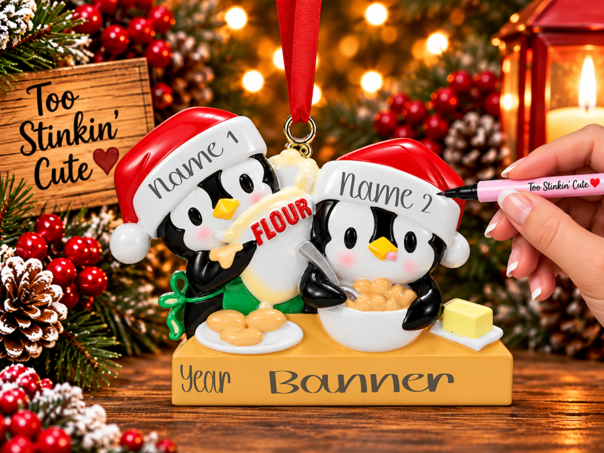 Penguin baking couple ornament with a flour bag, white mixing bowl, cookies, and yellow butter.