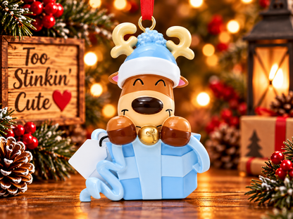 Front view of smiling reindeer peeking out of a blue present with sculpted ribbon and curled bow details.
