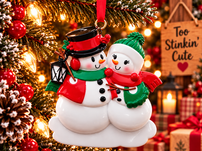 Snowman family of two ornament hanging from a red ribbon beside a wooden Too Stinkin’ Cute sign and warm Christmas lights.