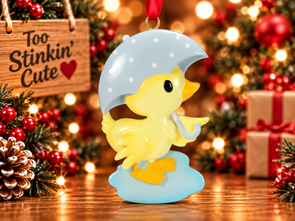 Yellow ducky personalized ornament hanging on a Christmas tree with warm holiday lights and greenery