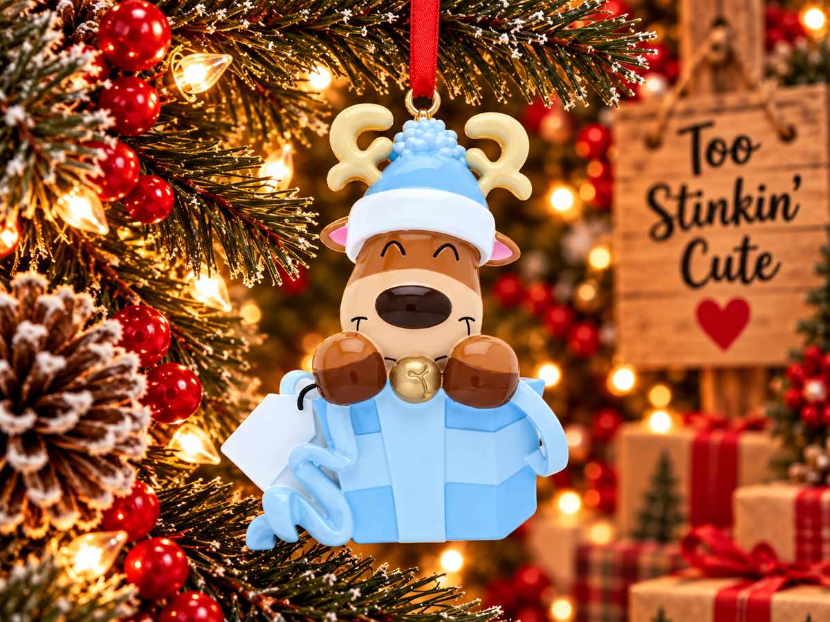 Reindeer Christmas ornament beside a Too Stinkin’ Cute wooden sign, evergreen branches, and red berries.