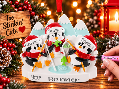 Penguin family of three ornament with orange fishing poles, green fish, and a light blue ice fishing hole.