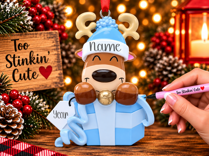 Brown reindeer ornament with cream antlers, a blue hat with white trim, and a gold-colored bell.