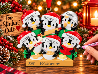 Penguin baking family of six ornament with a rolling pin, flour bag, mixing bowl, red recipe book, cookies, and butter.
