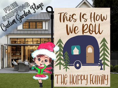 This Is How We Roll garden flag mockup with a navy camper, pine trees and family-name lettering on a wood-look background.