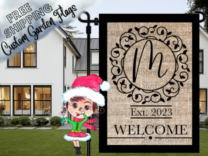 Burlap-look garden flag mockup with a black script monogram, ornate circular frame and welcome message.