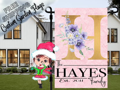 Pink garden flag mockup with a large gold H, purple flowers and Hayes family-name lettering.