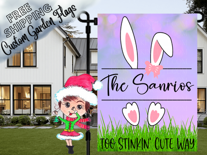 Purple garden flag mockup with white bunny ears and feet, a pink bow, green grass and family name.