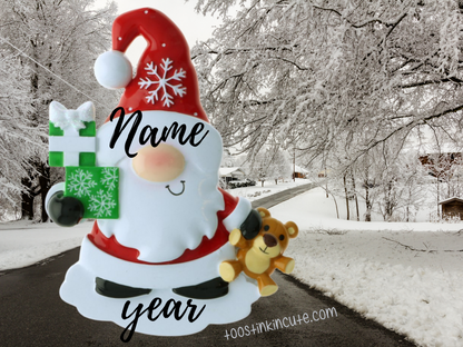 Christmas gnome with a red snowflake hat, white beard, present, and teddy bear, showing name and year placement.
