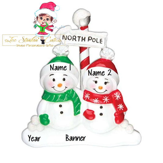 Family of 2 table topper with snowmen gathered around a striped North Pole sign. Sample personalization labels are shown.